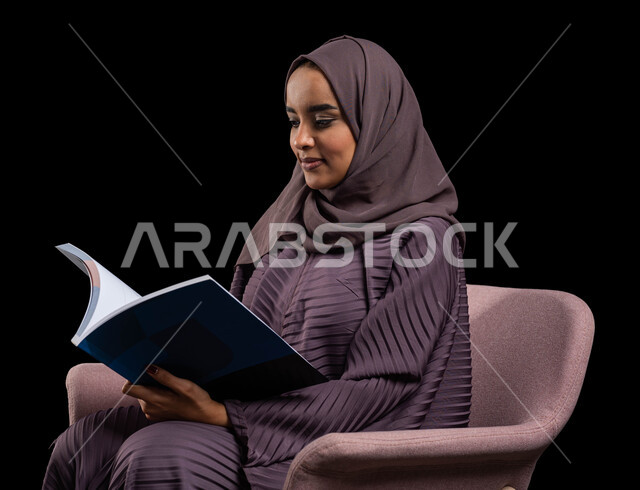 إنجاز الواجبات اليومية, قضاء الوقت بالقراءة والتعلم والتثقف ، بورتريه لامرأة عربية سعودية خليجية محجبة ترتدي العباءة تجلس على كرسي مريح وتحمل بيديها كتاب، الاستمتاع بقراءة الكتب والقصص والروايات, ثقافة التعلم الذاتي, خلفية سوداء.