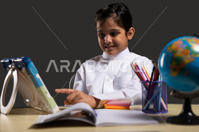 تفاعل الطلاب مع المحتوى التعليمي عبر الإنترنت، ايماءات الاندماج والتركيز،المذاكرة من خلال منصات التعليم الالكتروني، بورتريه مقرب لولد عربي سعودي خليجي يرتدي الزي السعودي التقليدي يقوم باستخدام التابلت، خلفية سوداء