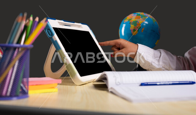 دمج التعليم مع التقنية، المقررات والمناهج التعليمية الحديثة والمطورة في السعودية، بورتريه مقرب من الجانب لتلميذة عربية سعودية خليجية ترتدي الزي المدرسي  تجلس على طاولة الدراسة وتقوم بالنقر على الجهاز اللوحي، خلفية سوداء.