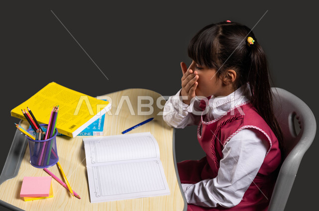 الحاجة للنوم وأخذ قسط من الراحة, الشعور بالكسل والخمول لحل الوظائف والواجبات المدرسية, بورتريه لبنت عربية سعودية خليجية ترتدي الثوب المدرسي تجلس أمام طاولة الدراسة تتثاءب وتضع يدها على فمها, إيماءات النعاس والإحساس بالتعب, العودة إلى المدارس, خلفية سوداء.