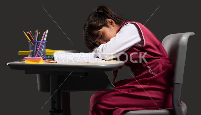 الشعور بالكسل والخمول اثناء حل الوظائف والواجبات المدرسية, الحاجة للنوم وأخذ قسط من الراحة, بورتريه لبنت عربية سعودية خليجية ترتدي الثوب المدرسي نائمة على طاولة الدراسة, إيماءات النعاس والإحساس بالتعب, العودة إلى المدارس, خلفية سوداء.