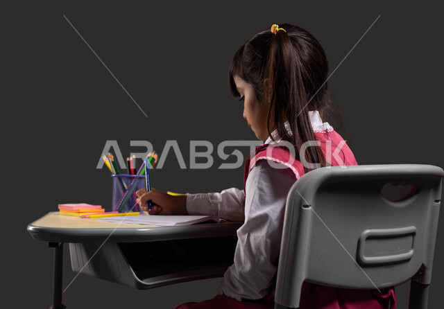 طلب العلا والمثابرة والحرص على النجاح، ايماءات تدل على التركيز والتفكير بالإجابة، بورتريه مقرب من الجانب لطالبة عربية خليجية سعودية ترتدي الزي المدرسي تجلس على الطاولة، المذاكرة للاختبارات والاستعداد للامتحان، خلفية سوداء.