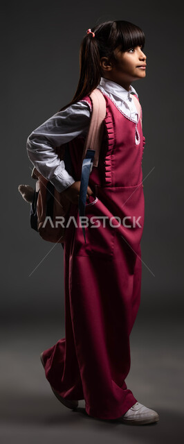 موسم العوده للمدارس, التهيئة والتجهيز لبداية العام الدراسي, بورتريه من الجانب لطالبة عربية خليجية سعودية ترتدي الزي المدرسي وتحمل الحقيبة المدرسية, تلميذه سعودية مجتهده ومتميزه, ايماءات المشي إلى المدرسه, صورة الجسم بالطول الكامل, خلفية سوداء.