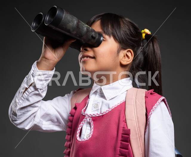 العودة إلى المدارس برؤية جديدة متطورة، جودة التعليم في المملكة العربية السعودية، بورتريه مقرب لتلميذة عربية خليجية سعودية ترتدي الزي المدرسي والحقيبة المدرسية تضع المنظار على عينيها لتقريب الاشياء البعيدة، الاستعداد للفصل الدراسي الجديد، خلفية سوداء.