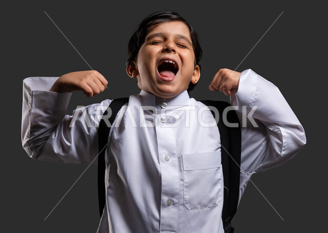 Feeling lazy and lethargic to go to school early, close-up portrait of a Saudi Gulf Arab boy wearing a school uniform and carrying a bag, yawning, sleepy gestures and a feeling of fatigue, the need for sleep and rest, returning to school, black background