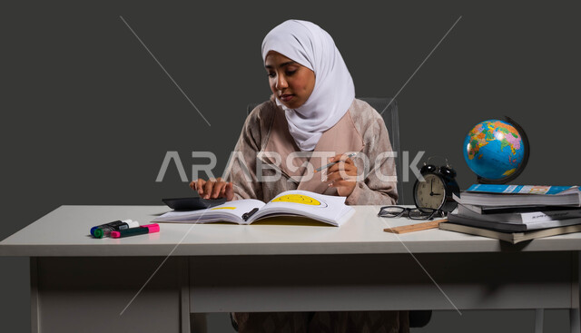إيماءات الاجتهاد والتركيز وحب العلم والتعلم , طالبة ثانوية تقوم بالتحضير للاختبارات النهائية, بورتريه مقرب لشابه عربية خليجية سعودية محجبة ترتدي العباءة وتجلس على كرسي مريح , الدقة والتمعن في إجراء العمليات الحسابية ,حل المسائل الرياضية والإحصائية ,   خلفية سوداء .