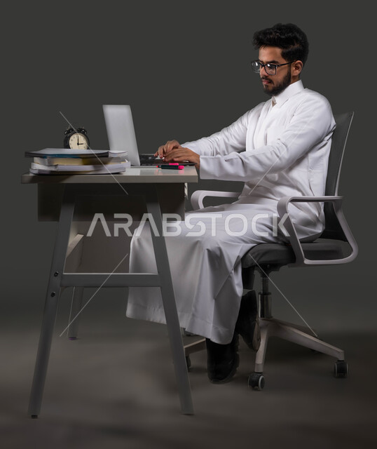 استخدام التكنولوجيا في المذاكره، بورتريه لطالب جامعي خليجي سعودي يرتدي الزي التقليدي وينظر الى شاشة الحاسب المحمول، التحول الرقمي في مدارس المملكة العربية السعودية، خلفية سوداء