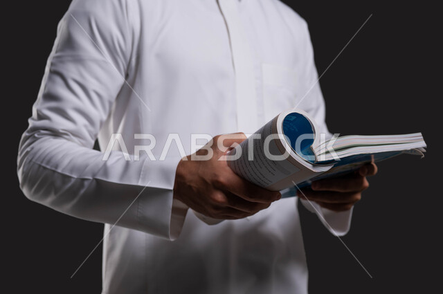 أهمية القراءة في توسيع آفاق المعرفة وزيادة المعلومات، دور التعليم في تطوير المجتمع السعودي، بورتريه مقرب لطالب ثانوي عربي خليجي سعودي مبتسم يرتدي الزي التقليدي ويقرأ من كتابه المدرسي، العلم مفتاح التطور والنجاح، خلفية سوداء.