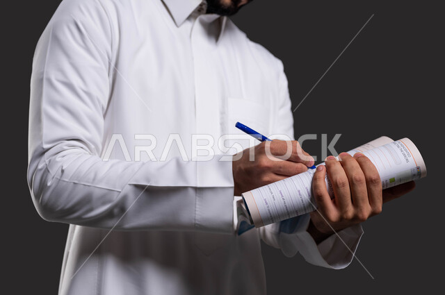 دور المدارس في بناء القيم والأخلاق الحسنه للطلاب، تطوير المناهج والمواد التعليمية في السعوديه، العودة الى المدارس، بورتريه مقرب لطالب ثانوي عربي خليجي سعودي يرتدي الزي التقليدي ويكتب على الدفتر، خلفية سوداء.