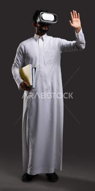 جودة التعليم المتطور باستخدام تقنية العالم الافتراضي في السعودية, تعزيز التفاعل والمشاركة في الفصول الدراسية، بورتريه لطالب ثانوي عربي خليجي سعودي يرتدي الزي التقليدي يضع نظارات في آر ويرفع يده لالقاء التحية، صورة الجسم بالطول الكامل، خلفية سوداء.