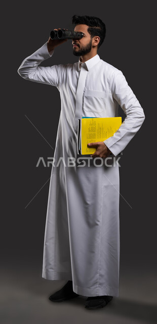 البحث عن شيء، رؤية مستقبلية للتعليم، بورتريه مقرب لطالب جامعي خليجي سعودي يرتدي الزي التقليدي وينظر من خلال المنظار،  استخدام البرامج والتطبيقات الرقمية في التعلم، العودة الى المدارس، خلفية سوداء