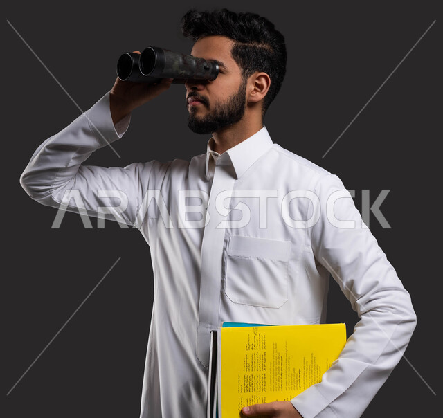 A future vision for education, a close-up portrait of a Saudi Gulf high school student wearing traditional clothing and looking through binoculars, searching for something, using digital programs and applications in learning, returning to school, black background