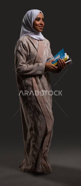The role of schools in raising generations capable of taking responsibility and developing society, portrait of a veiled Saudi Arabian Gulf high school student wearing a colorful abaya and holding school books in her hand, the importance of education in building a bright future for Saudi society, full-length body image, black background