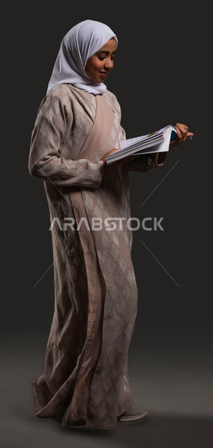 Developing curricula and educational materials in Saudi Arabia, portrait of a veiled Saudi Arabian Gulf high school student wearing a colorful abaya and holding school books in her hand, the importance of education in building a bright future for Saudi society, full-length body image, black background