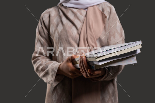 The role of schools in developing human values and morals among students, a close-up portrait of a Saudi Arabian Gulf high school student wearing a colorful abaya and holding school books in her hand, the importance of education in building a bright future for Saudi society, black background.