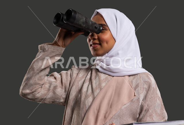 نشاطات لتحفيز العقل والفكر, التطلع للطموحات والأهداف المستقبلية باستخدام المنظار ثنائي العينين, بورتريه مقرب لطالبة ثانوية عربية خليجية سعودية مبتسمة محجبة ترتدي العباءة وتضع منظار الرؤية, إيماءات الاستمتاع والسرور, خلفية سوداء .