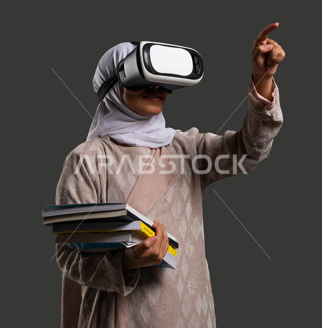 فوائد استخدام نظارات الواقع الافتراضي في عملية التعلم، التحول الرقمي في مدارس المملكة العربية السعودية، بورتريه لطالبة ثانوي عربية سعودية خليجية محجبة ترتدي عباءة وترفع اصبعها متفاعلة مع المحتوى الافتراضي، خلفية سوداء.