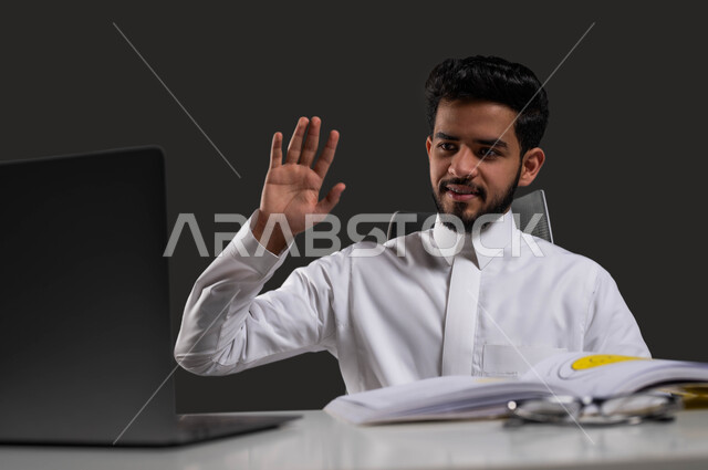 تفاعل الطلاب مع المحتوى التعليمي عبر الانترنت، المقررات والمناهج التعليمية الحديثة والمطورة بالسعودية، بورتريه لطالب جامعي عربي خليجي سعودي يرتدي الزي التقليدي يجلس أمام الطاولة الدراسية وجهاز الحاسوب، خلفية سوداء.