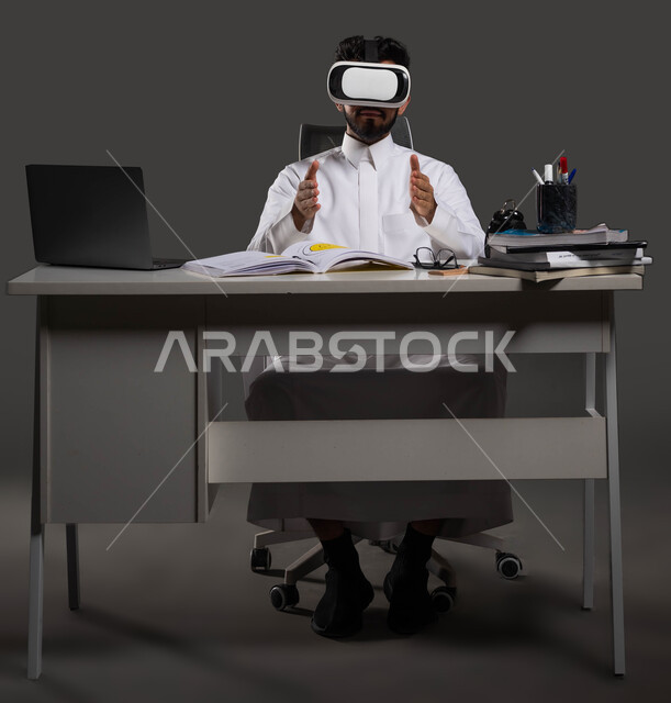جودة التعليم المتطور باستخدام تقنية العالم الافتراضي في السعودية، دور نظارات الواقع الافتراضي في تعزيز التفاعل والمشاركة في الفصول الدراسية، بورتريه لطالب جامعي سعودي يرتدي الزي التقليدي ويشير بيديه إلى الأمام بإيماءات التحجيم والإمساك بعنصر ما، خلفية سوداء.