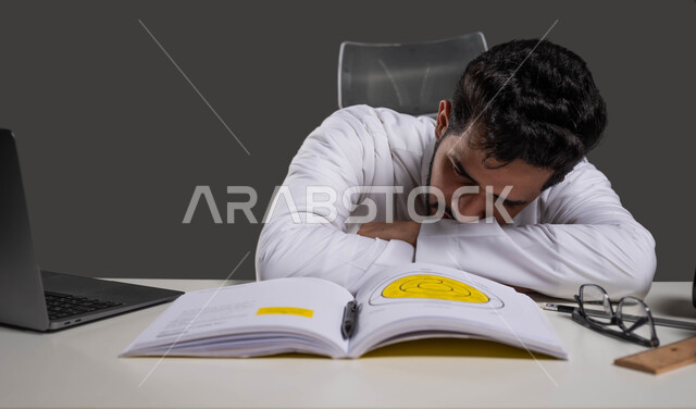 التعب والاجهاد اثناء مراجعة الدروس اليومية، المذاكرة لأوقات متاخرة من الليل، السعي للتفوق والنجاح، بورتريه مقرب لطالب ثانوي عربي خليجي سعودي يرتدي الزي التقليدي نائم على طاولة الدراسة، التعليم في المملكة العربية السعودية، خلفية سوداء.