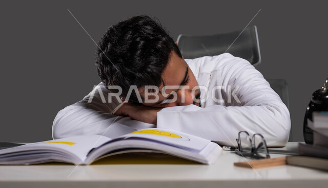 التعب والاجهاد اثناء مراجعة الدروس اليومية، المذاكرة لأوقات متاخرة من الليل، السعي للتفوق والنجاح، بورتريه مقرب لطالب ثانوي عربي خليجي سعودي يرتدي الزي التقليدي نائم على طاولة الدراسة، دخول وقت النوم، خلفية سوداء.