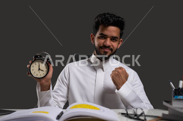 دور المدارس في تنشئة الأجيال القادرة على تحمل المسؤولية وتطوير المجتمع، ايماءات الإنجاز الدراسي وتحقيق الأهداف في الوقت المناسب، بورتريه مقرب لطالب جامعي عربي خليجي سعودي مبتسم يرتدي الزي التقليدي ويرفع قبضة يده للأعلى، العلم مفتاح التفوق والنجاح، خلفية سوداء.