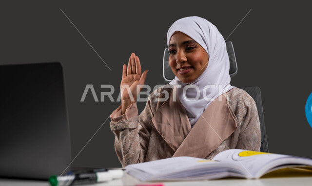 التعلم التفاعلي عبر الانترنت، بورتريه مقرب لطالبة ثانوية خليجية سعودية ترتدي العباءة تجلس أمام طاولة الدراسة وتشارك بالحصة الدراسية مع المعلم من خلال الحاسب المحمول، استخدام البرامج والتطبيقات الرقمية في التعلم، العودة الى المدارس، خلفية سوداء.