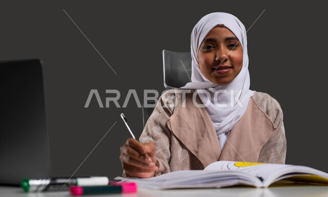 مفهوم الدراسة بجد واجتهاد, بورتريه مقرب لطالبة جامعية عربية خليجية سعودية محجبة ترتدي العباءة تنظر إلى الكاميرا بإيماءات السرور, جودة التعليم المنزلي في المملكه العربيه السعوديه، خلفية سوداء.
