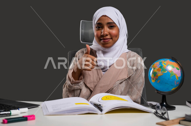 The concept of studying hard and diligently, a close-up portrait of a veiled Saudi Gulf Arab university student wearing an abaya and raising her thumb up, gestures of acceptance and approval, and the quality of home education, a black background.