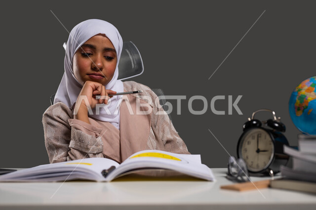 الشعور بالكسل والملل أثناء مراجعة الدروس، بورتريه لطالبة ثانوية عربية خليجية سعودية محجبة ترتدي العباءة تنظر إلى الكتاب بإيماءات التفكير والتركيز, أهمية التعليم في المملكة العربية السعودية في بناء مستقبل مشرق للطلاب، خلفية سوداء.