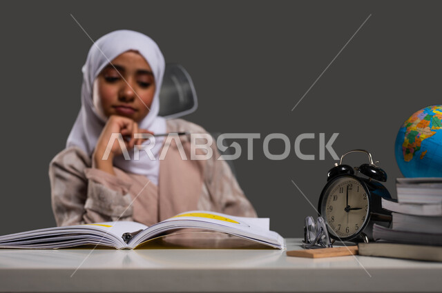 تطوير المناهج والمواد التعليمية في المملكة العربية السعودية، الشعور بالكسل والملل أثناء مراجعة الدروس، بورتريه لطالبة ثانوية عربية خليجية سعودية محجبة ترتدي العباءة تنظر إلى الكتاب بإيماءات التتفكير والتركيز, خلفية سوداء.