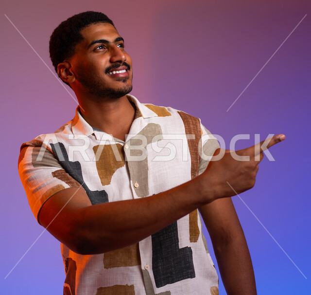 حركات تدل على الذهاب إلى مكان ما، التأمل وتحديد الأهداف، بورتريه مقرب لرجل عربي خليجي سعودي مبتسم يرتدي الزي الكاجوال يشير بأصابعه نحو اليمين بإيماءات السرور، مفهوم لغة الجسد وتعابير الوجه، خلفية ملونة