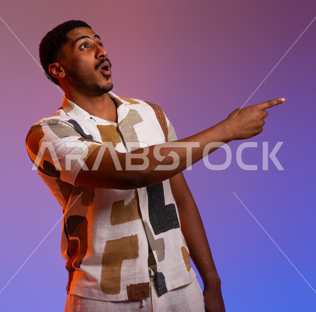 الشعور بالصدمة والذهول، حركات ودلالات مختلفة، بورتريه لرجل عربي خليجي سعودي يرتدي الزي الكاجوال يشير بأصابعه نحو اليمين بإيماءات التعجب والاندهاش من شيء ما، الاستغراب من أمر معين، خلفية ملونة