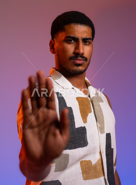 الصمت والتوقف عن الكلام، إيماءات يدين تدل على الأمر بالتوقف عن فعل شيء ما و النهي عنه, بورتريه مقرب لرجل عربي سعودي خليجي يرتدي الزي الكاجوال ويرفع كفه للأعلى, الشعور بالإنزعاج و الرفض والإمتناع، خلفية ملونة