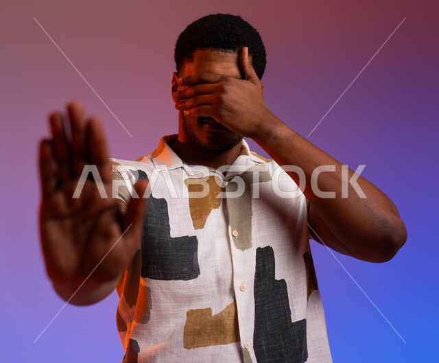 الحزن والإحباط و الرغبه بالبكاء, بورتريه لرجل عربي خليجي سعودي يرتدي الزي الكاجوال يرفع كفه للأعلى, الشعور بالخيبه والامتناع عن رؤية الأمر السيء, إيماءات طلب التوقف عن فعل شيء ما و النهي عنه, الإحساس بالانزعاج و الرفض والفشل. خلفية ملونة