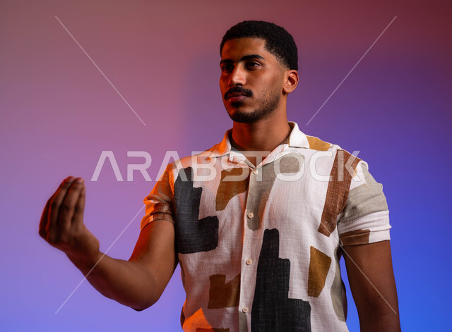 مفهوم الصبر والتريث و التأني, التهديد و التوعد لشيء ما، بورتريه مقرب لشاب عربي سعودي خليجي يرتدي الزي الكاجوال يرفع يده نحو الأعلى بإيماءات طلب الإنتظار والتمهل, إمهال بعض الوقت لفعل شيء، خلفية ملونة.