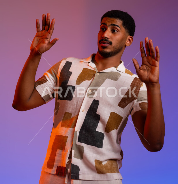 القلق والاحتياط والابتعاد عن شيء ما، حماية النفس من ضرر خارجي, بورتريه مقرب لرجل عربي خليجي سعودي يرتدي الزي الكاجوال و يرفع يديه بإيماءات التوقف وعدم الاقتراب, الشعور بالانزعاج وعدم الراحة،  خلفية ملونة