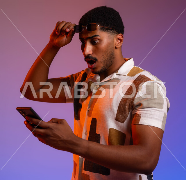 الفشل في تحقيق الاهداف، رؤية الأخبار السيئة على مواقع التواصل الاجتماعي، بورتريه مقرب لرجل عربي سعودي خليجي يرتدي الزي الكاجول يمسك بيده الجوال يقوم برفع نظارته الشمسية، ايماءات الصدمة  والدهشة والاستغراب، خلفية ملونة