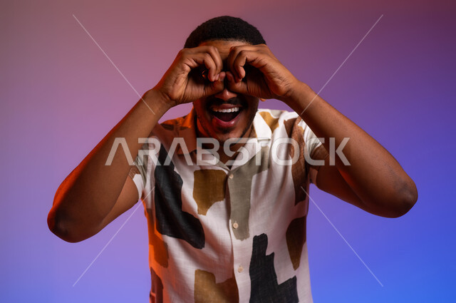 التخطيط المستقبلي للأهداف والطموحات، بورتريه مقرب لشاب عربي سعودي خليجي مبتسم يرتدي الزي الكاجوال يضع يده على عينه كالناظور، ايماءات الحماس بالبحث عن شيء ما، رؤية الفرص والتحديات المحتملة، خلفية ملونة