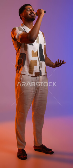 القاء الخطابات والحوارات، تقديم العروضات المسرحية، الفن المسرحي الغنائي، ممارسة هواية الغناء للتسلية والترفيه، بورتريه لشاب عربي سعودي خليجي مبتسم يرتدي الزي الكاجوال يحمل بيده الميكروفون، مواهب فنية في عالم الموسيقى، صورة الجسم بالطول الكامل، خلفية ملونة