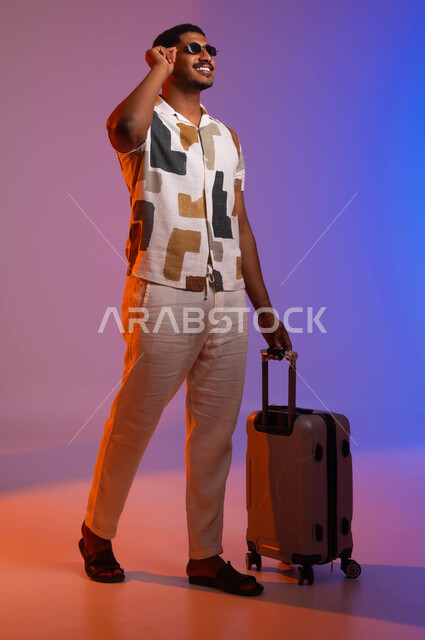 جولة استكشاف ثقافات وعادات جديدة، بورتريه لرجل عربي سعودي خليجي مبتسم يرتدي قميص صيفي يضع النظارة الشمسية ويمسك بيده حقيبة السفر، السفر كوسيلة  للاسترخاء والترفيه عن النفس، صورة الجسم بالطول الكامل، خلفية ملونة