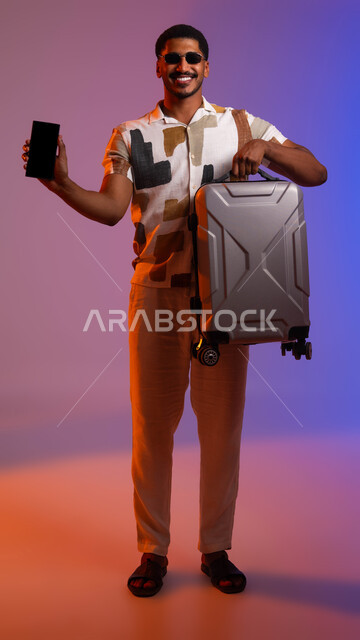 استخدام التكنولوجيا المتطورة, بورتريه لرجل عربي سعودي خليجي يرتدي الزي الكاجوال والنظارة الشمسية يمسك بيده الهاتف المحمول بشاشة سوداء فارغة, عرض تطبيقات وبرامج التواصل الاجتماعي, صورة الجسم بالطول الكامل,  خلفية ملونة.