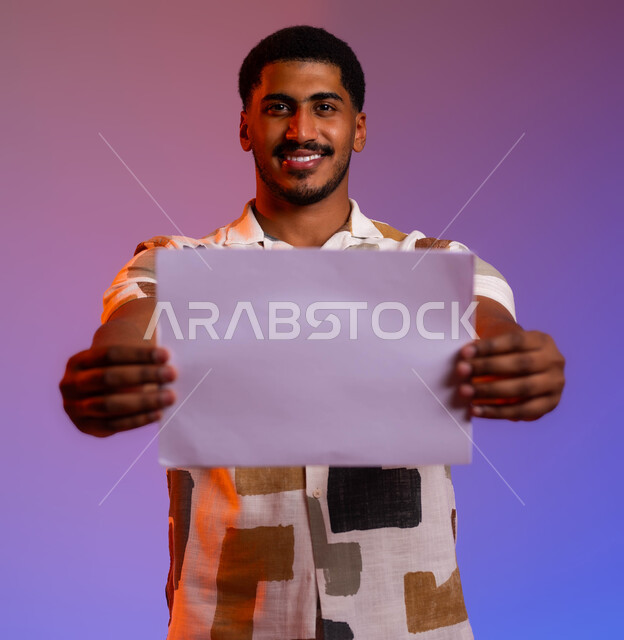 دراسة جدول لمشروع، مراجعة وتدقيق الخطط المكتبية, بورتريه مقرب لشاب عربي خليجي سعودي مبتسم يقوم بعرض ورقة بيضاء فارغة إيماءات الفرح بزيادة الأرباح وتحقيق الأهداف، مراسلات وسجلات خاصة بالعمل, خلفية ملونة.