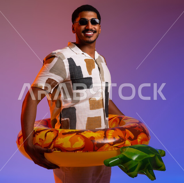 A fun youth trip on the seashore in the summer, a portrait of a smiling Saudi Arabian Gulf man wearing casual clothes and sunglasses and looking at the camera, wearing a water buoy to relax, preparing to practice swimming, feeling enjoyment in recreational activities, colorful background