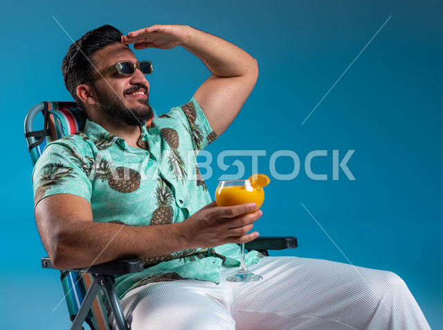 الاستمتاع بالجلسات االهادئة والنظر إلى شيء ما, بورتريه لشاب عربي خليجي سعودي مبتسم يرتدي الزي الكاجوال والنظارة الشمسية يجلس على الكرسي في إحدى الشواطئ والمتتجعات الترفيهيه, رفع اليد للأعلى والحماية من أشعة الشمس, شرب العصائر الطبيعيه المنعشة, خلفية زرقاء