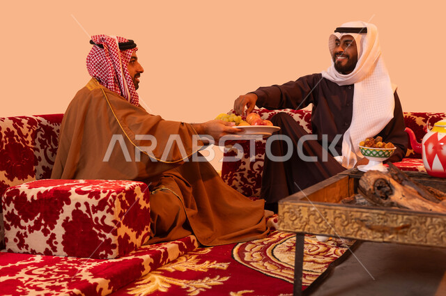 تبادل الحكايا مع الأصدقاء، تقاليد وثقافة المجتمع السعودي في حسن الضيافة والكرم، بورتريه لرجل عربي خليجي سعودي يرتدي الزي التقليدي يقوم بتقديم الضيافة، جلسات سعودية تقليدية في الهواء الطلق، مفهوم الكشتة البرية، خلفية بيج