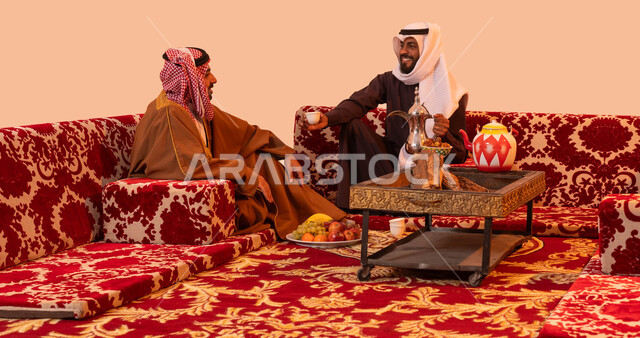 كشتة برية شبابية، حورارات ونقاشات بين الأصدقاء، بورتريه لرجلان عربيان خليجيان سعوديان يرتديان الزي التقليدي يتبادلان الحديث يتسامران، تقديم القهوة السعودية في الجلسات الخارجية، إيماءات البشاشة وحسن الاستقبال، خلفية بيج.