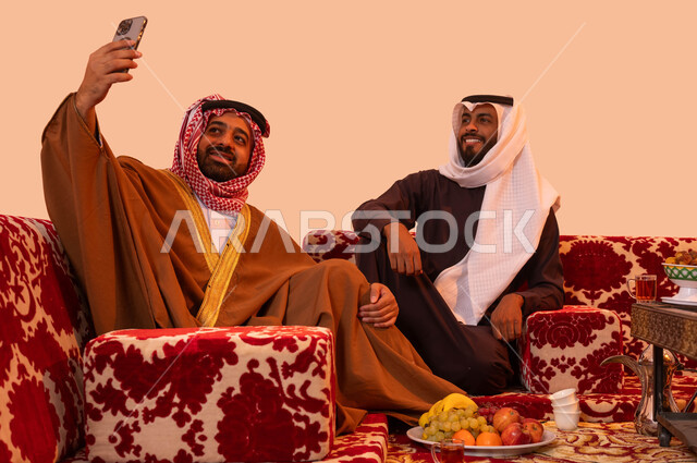 الاهتمام بالضيوف أثناء الكشتة البدوية،  استخدام تطبيقات وبرامج الهاتف المحمول، بورتريه لرجلان عربيان خليجيان سعوديان  يقومان بالتقاط صورة تذكارية، استنشاق الهواء النقي والنظيف، مفهوم حسن الضيافه والكرم، جلسات شعبية خارجية مع الأصدقاء، خلفية بيج