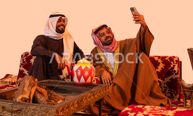 عادات سعودية اصيلة في حسن الضيافه والكرم، استخدام التقنية الحديثة، بورتريه لشباب عرب خليجية سعودية يقومون بتوثيق اللحظات السعيدة باستخدام الهاتف المحمول، مفهوم الجلسات الشعبية البرية، فعاليات وأجواء ترفيهية، الاستمتاع بالهواء العليل والجلسات المفتوحة، خلفية بيج