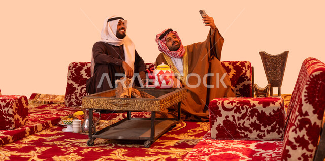 الاهتمام بسعادة وراحة الضيوف، استخدام تطبيقات وبرامج الهاتف المحمول، بورتريه لرجلين عربيين خليجيين سعوديين يقومان بالتقاط صورة تذكارية، استنشاق الهواء النقي والنظيف أثناء الكشتة البرية، مفهوم حسن الضيافه والكرم، جلسات شعبية خارجية مع الأصدقاء، خلفية بيج